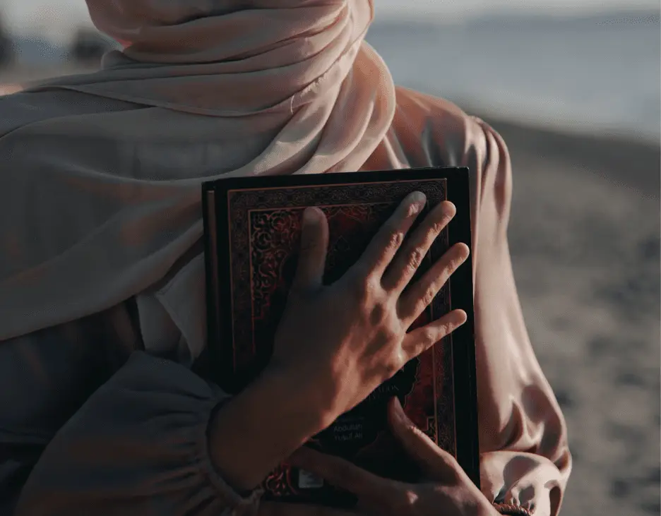 Une femme portant un hijab, serrant un Coran contre elle, face à la mer