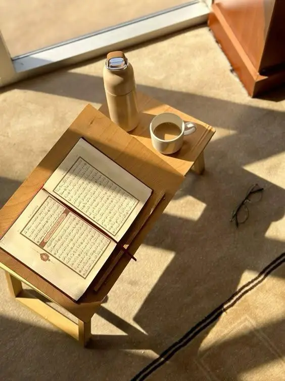 Un Coran ouvert sur une table basse baignée de lumière, avec une tasse de café